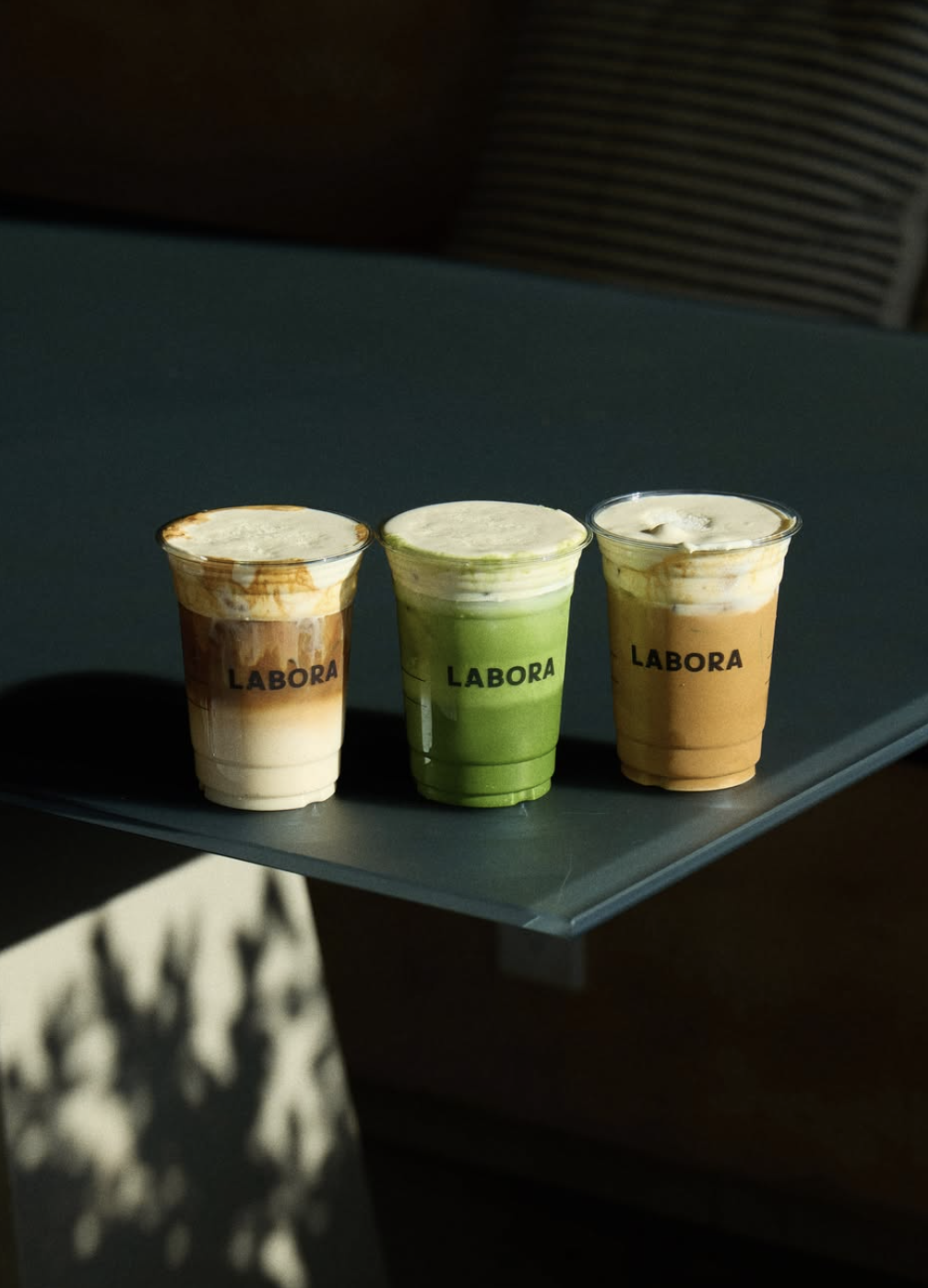 Three iced Labora drinks in branded cups — coffee, matcha, and a foam-layered latte